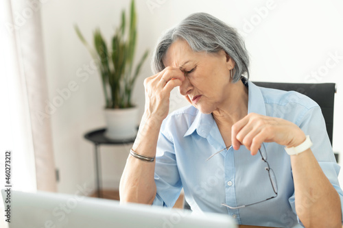 Tired and overworked stressed mature woman working on laptop at home indoor, female teacher feeling exhausted after lecturing students online, touching eyes. Smart working senior people and technology