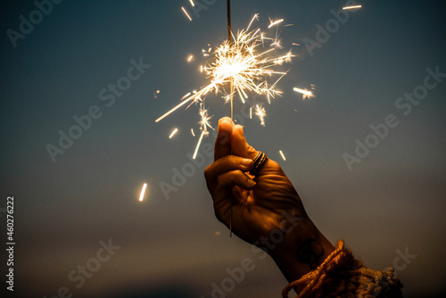 Photography Hand holding sparkler firework firing with sunset sky in background - concept of