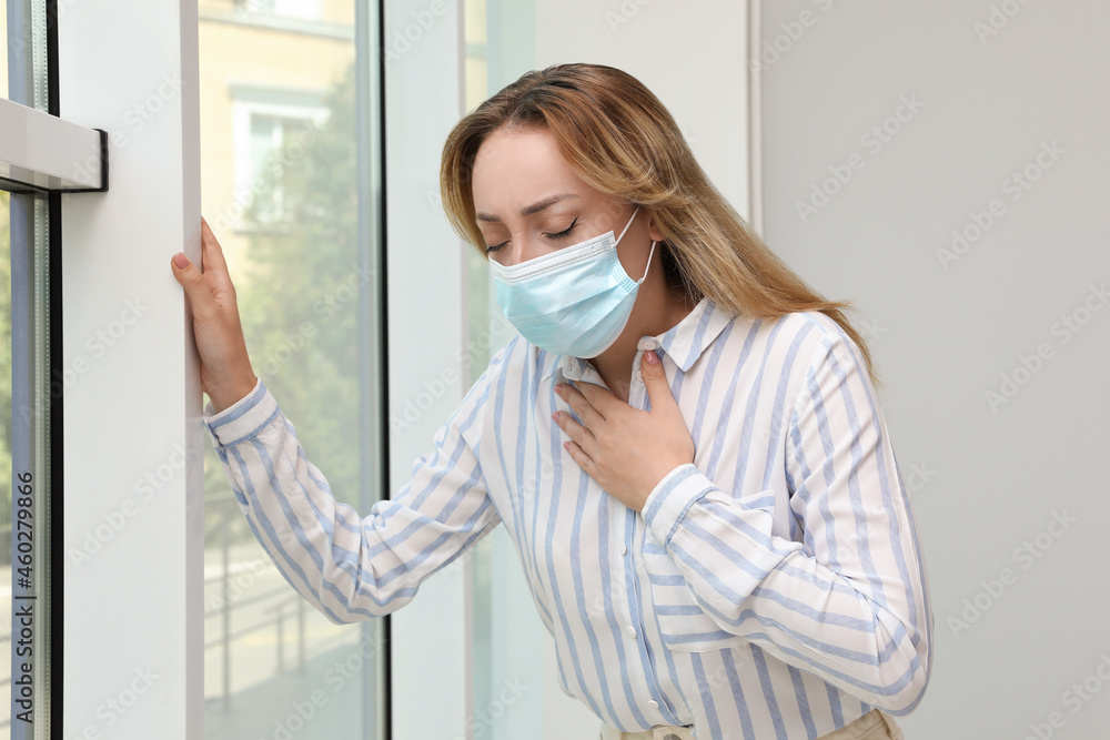Young woman in medical mask suffering from pain during breathing near window Young woman in medical mask suffering from pain during breathing near window