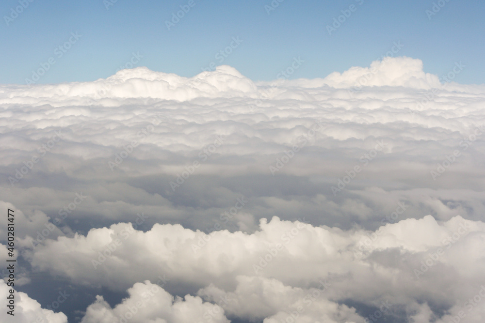 Naklejka premium View of above clouds from airplane window with blue sky background. Use for wallpaper or backdrop.