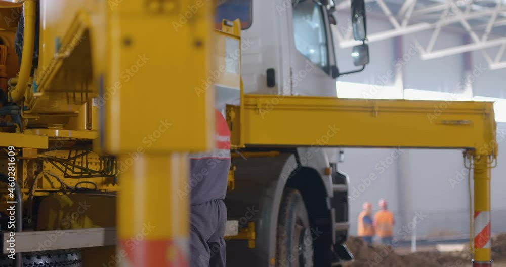 At a construction site, a powerful mobile crane is preparing to lift a load, operator extends outriggers for work At a construction site, a powerful mobile crane is preparing to lift a load, operator extends outriggers for work