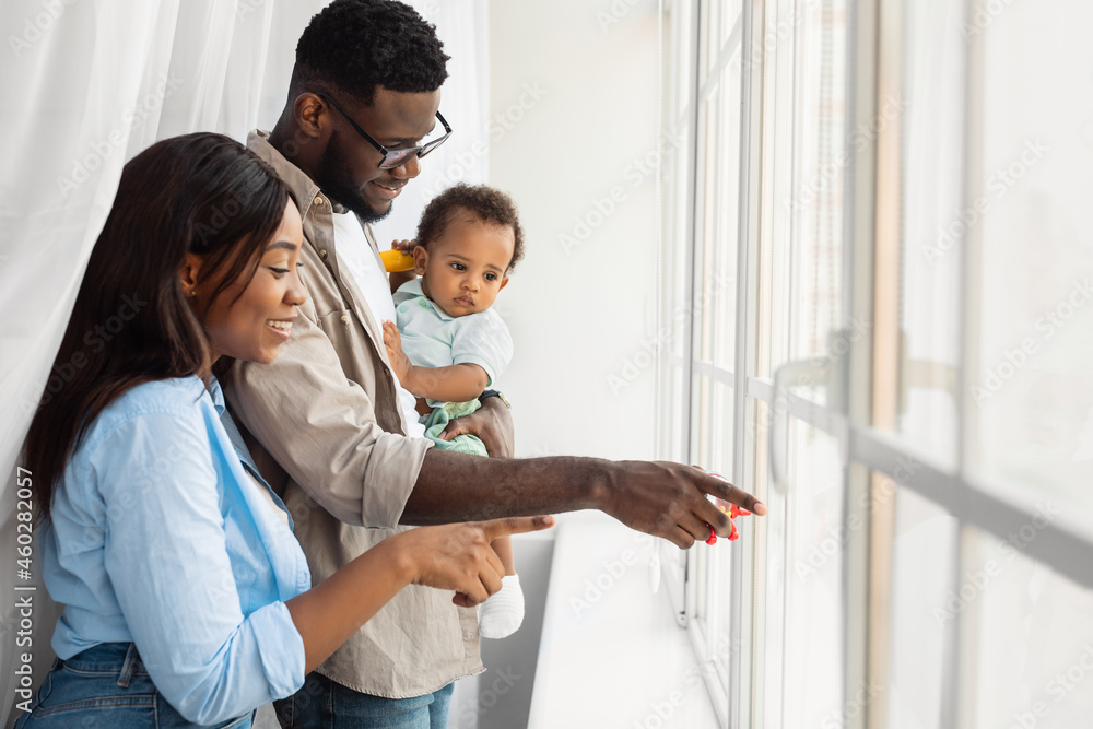 Happy black parents holding baby pointing at window