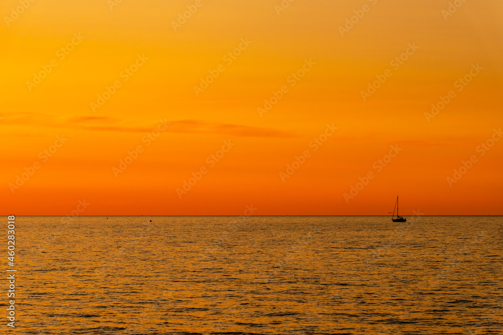 Orange and yellow sunset on the sea with a sailboat. Minimalistic photo of a silhouette of sailing boat on the sea during dusk.