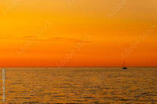 Orange and yellow sunset on the sea with a sailboat. Minimalistic photo of a silhouette of sailing boat on the sea during dusk. © Evelyn