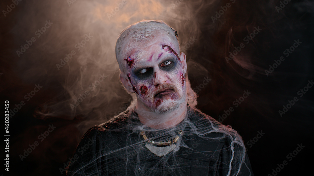 Frightening man with Halloween zombie bloody wounded makeup, trying to scare, face expressions. Convulsions. Sinister undead guy isolated on studio black background. Voodoo rituals. Fashion body art Frightening man with Halloween zombie bloody wounded makeup, trying to scare, face expressions. Convulsions. Sinister undead guy isolated on studio black background. Voodoo rituals. Fashion body art