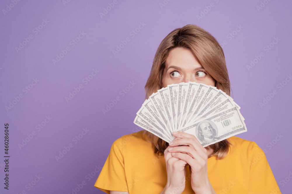 Photo of young attractive woman closing face dollars banknotes cash look empty space isolated over violet color background Photo of young attractive woman closing face dollars banknotes cash look empty space isolated over violet color background