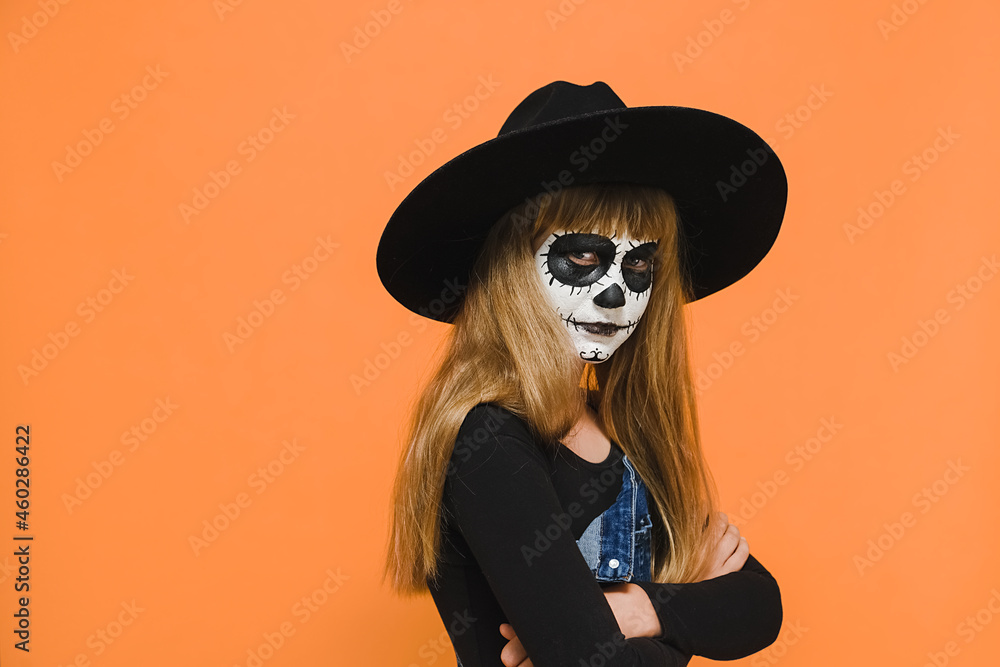 Angry sad little blonde girl kid with Halloween spooky makeup mask, wears black hat, crossed arms, unhappy looking at camera, posing isolated over orange color background wall studio with copy space Angry sad little blonde girl kid with Halloween spooky makeup mask, wears black hat, crossed arms, unhappy looking at camera, posing isolated over orange color background wall studio with copy space