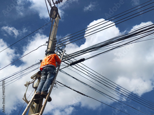 the technician on wooden ladder checking fiber optic cables  on electric pole at workplace with messy electrical wire cables on lightpost against blue sky background , technology, unsafety concept.
