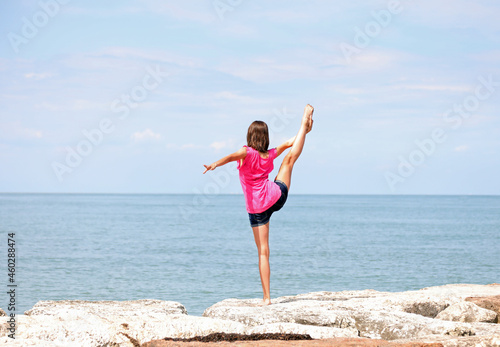 caucasian girl performing rhythmic gymnastics exercises with the leg up and the foot over the head in summer