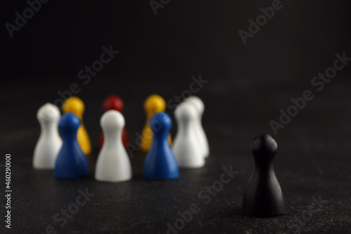 Black pawn standing out from other ones on dark background, closeup. Racism concept