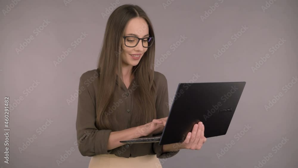 Attractive serious business woman 30 years old in a dark green office shirt. Woman working on a laptop while standing on a gray background. Attractive serious business woman 30 years old in a dark green office shirt. Woman working on a laptop while standing on a gray background.