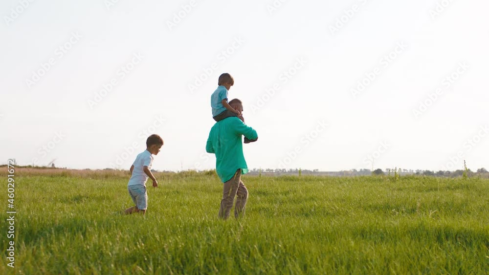 Young man and his cute small boys walking through the green field at nature they speeding time together discussing and looking to the landscape Young man and his cute small boys walking through the green field at nature they speeding time together discussing and looking to the landscape