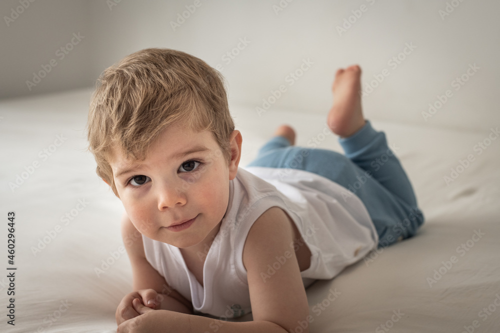 Niño rubio sonriendo a la cámara y jugando en la cama Niño rubio sonriendo a la cámara y jugando en la cama