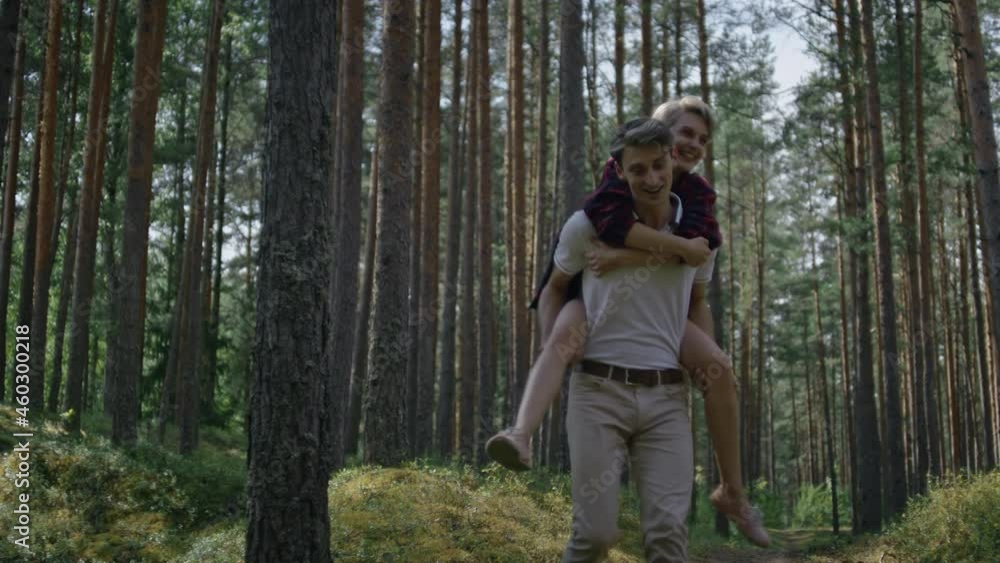 Soft focus handheld shot of young couple happy in love, have fun on forest walk. Boyfriend and girlfriend riding piggy back in warm summer light. Young woman laugh and smile in arms of partner Soft focus handheld shot of young couple happy in love, have fun on forest walk. Boyfriend and girlfriend riding piggy back in warm summer light. Young woman laugh and smile in arms of partner
