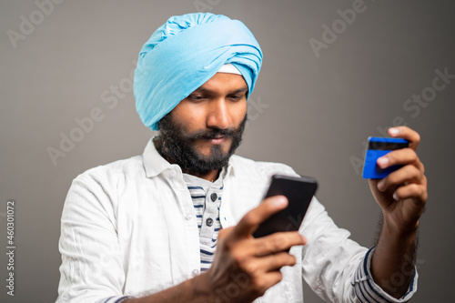 Young sikh man purchasing by paying online using credit card in mobile phone - concept of Online shopping or ordering from e-commerce. © WESTOCK