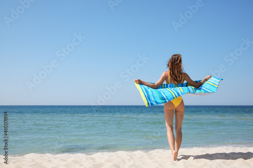 Woman with beach towel near sea on sunny day, back view