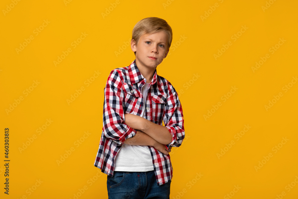 Serious sad calm teen caucasian boy pupil in shirt with crossed arms on chest, isolated on yellow background Serious sad calm teen caucasian boy pupil in shirt with crossed arms on chest, isolated on yellow background