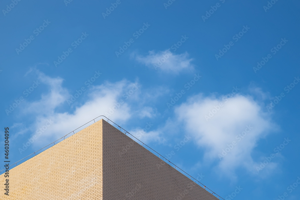 Part of the light yellow building under the blue sky and white clouds Part of the light yellow building under the blue sky and white clouds
