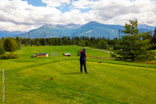 Golfer Teeing Off on Crans Sur Sierre Golf Course with House and Mountain View in Crans Montana in Valais, Switzerland.