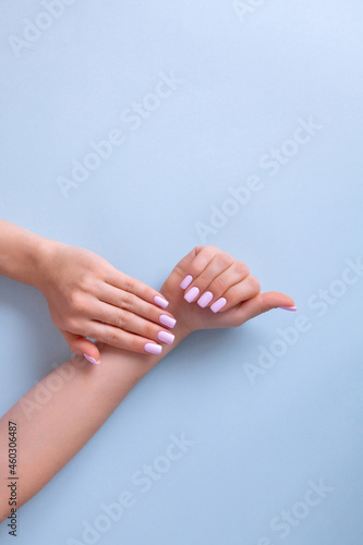 Hands of a beautiful woman on a blue background. Delicate hands with natural pink manicure, clean skin.