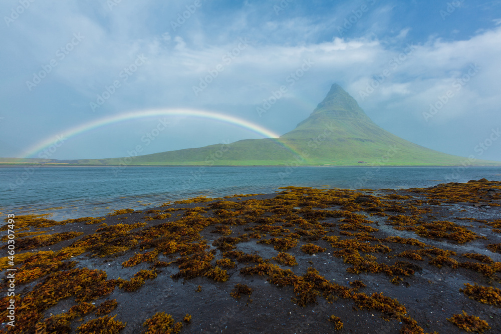 Kirkjufellsfoss with a rainbow from a beach 
