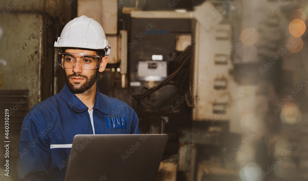 Professional handsome male engineer in blue uniform and helmet working on a laptop computer in the indoor field of a mechanical factory. Professional handsome male engineer in blue uniform and helmet working on a laptop computer in the indoor field of a mechanical factory.