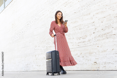 Cheerful female walking with suitcase against white wall photo