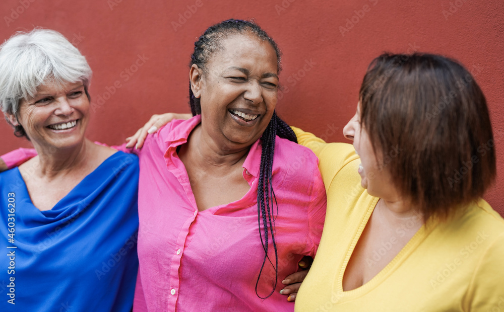 Multiracial mature women hugging each other in the city with red wall in background - Elderly people and friendship concept Multiracial mature women hugging each other in the city with red wall in background - Elderly people and friendship concept