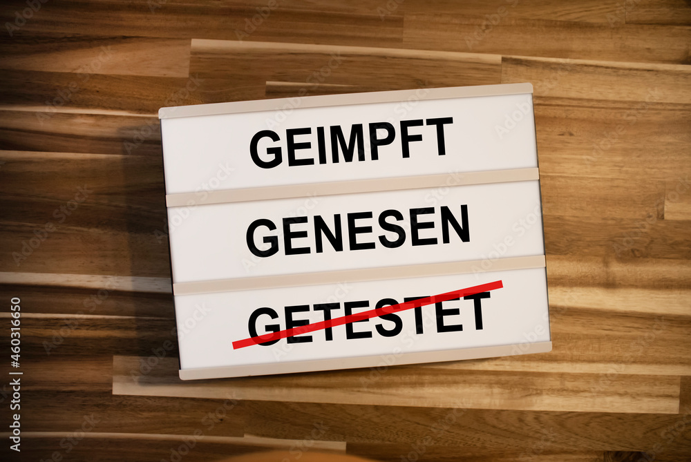 Lightbox or light box with german words for vaccinated, recovered or testet - geimpft, genesen, getestet on wooden table background
