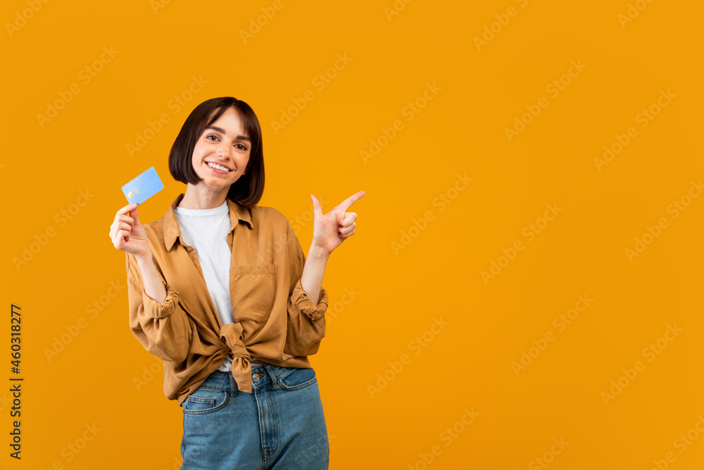 Excited lady with credit card pointing aside at empty space on yellow studio background, panorama Excited lady with credit card pointing aside at empty space on yellow studio background, panorama