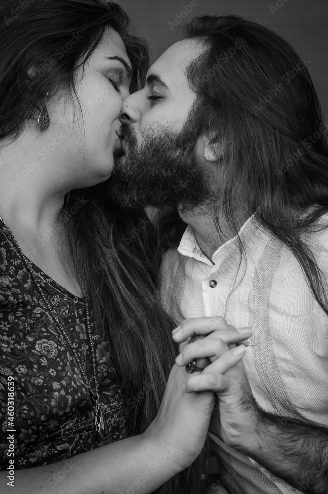 Black and white portrait of a young couple kissing holding hands, both have long hair and the man has a beard Black and white portrait of a young couple kissing holding hands, both have long hair and the man has a beard