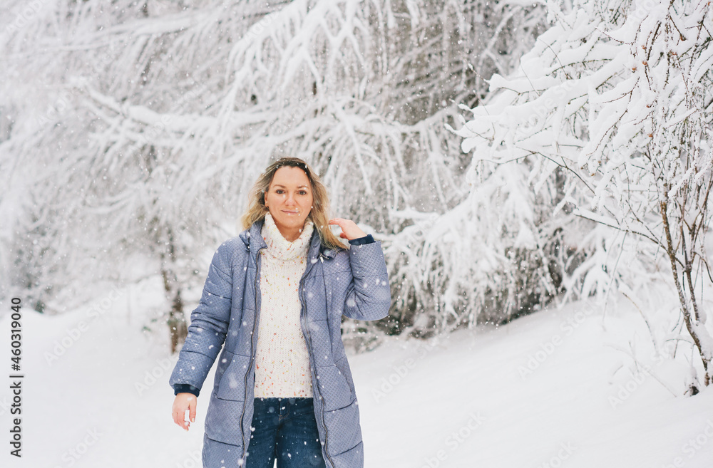 Happy mature woman enjoying nice winter day, wearing warm white pullover and blue winter jacket, standing under snowfall Happy mature woman enjoying nice winter day, wearing warm white pullover and blue winter jacket, standing under snowfall