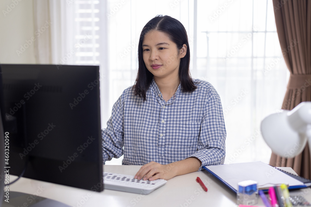 A portrait of a happy, middle-aged, long hair Asian woman working at home, using pc computer, looking at the screen, typing, and smiling. Remote working and technology concept. A portrait of a happy, middle-aged, long hair Asian woman working at home, using pc computer, looking at the screen, typing, and smiling. Remote working and technology concept.