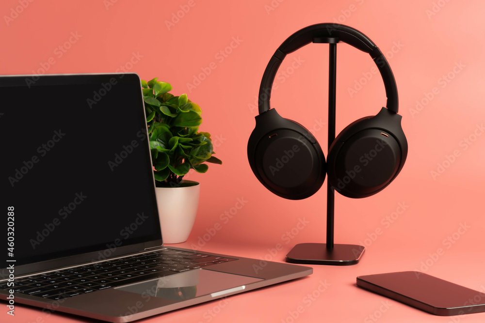 Black headphones hang on a table. Concept of playing music with a smartphone and listening with wireless headphones in the living room and Work at home. studio. Selective focus. pink background. Black headphones hang on a table. Concept of playing music with a smartphone and listening with wireless headphones in the living room and Work at home. studio. Selective focus. pink background.