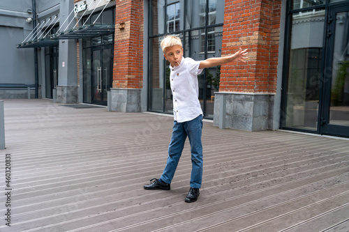 Cute fashionable boy standing on wooden podium and looking aside outdoors in city. Kid resting in free time, walk in downtown, look aside. Concept of urban lifestyle.
