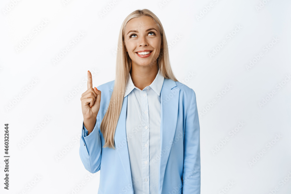 Portrait of young ceo office girl pointing and looking up, smiling pleased, reacing promo text, showing company logo, standing over white background Portrait of young ceo office girl pointing and looking up, smiling pleased, reacing promo text, showing company logo, standing over white background
