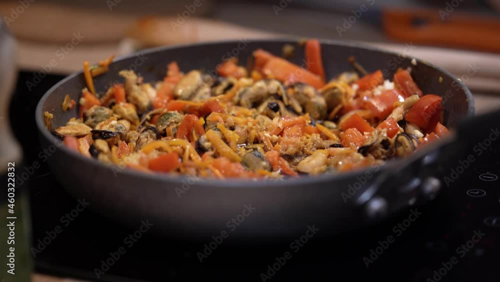 Hands poured sauce into frying pan with seafood and vegetables. Shrimp, mussels, carrots and bell peppers are stewed on stove. Dish of Asian cuisine for menu of restaurants and cafes. Hands poured sauce into frying pan with seafood and vegetables. Shrimp, mussels, carrots and bell peppers are stewed on stove. Dish of Asian cuisine for menu of restaurants and cafes.