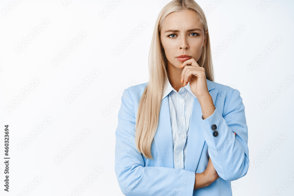 Image of concerned serious corporate woman, looking at camera while thinking, standing in suit over white background Image of concerned serious corporate woman, looking at camera while thinking, standing in suit over white background