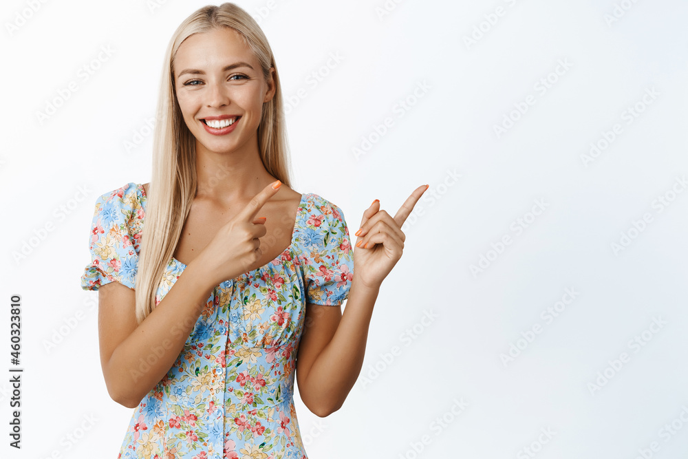 Cute blond girl smiles, points at upper right corner, shows advertisement, announcement or logo, stands against white background Cute blond girl smiles, points at upper right corner, shows advertisement, announcement or logo, stands against white background