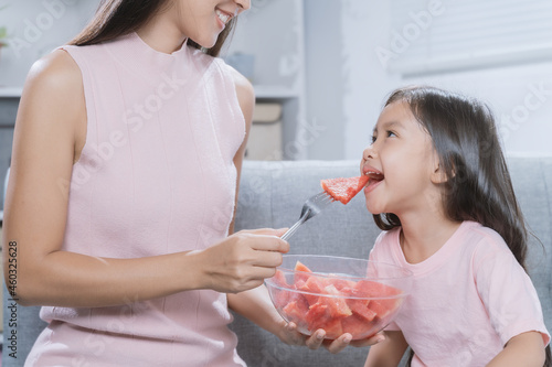 Mother is feeding her daughter a watermelon to eat.