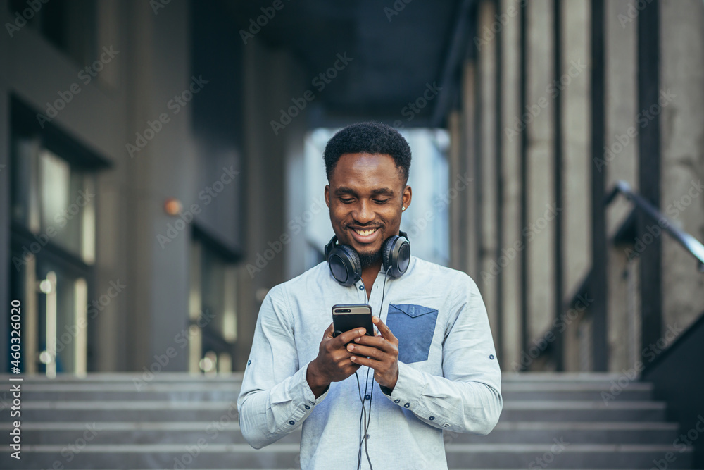 Φωτογραφία Young african american man happy with win looks at phone rejoices and smiles in