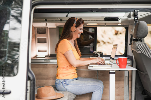 Mature woman working inside mini van camper with computer laptop wearing wireless headphone