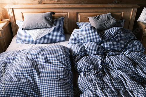 фотографія blue white chequered used bedclothes on wooden bed