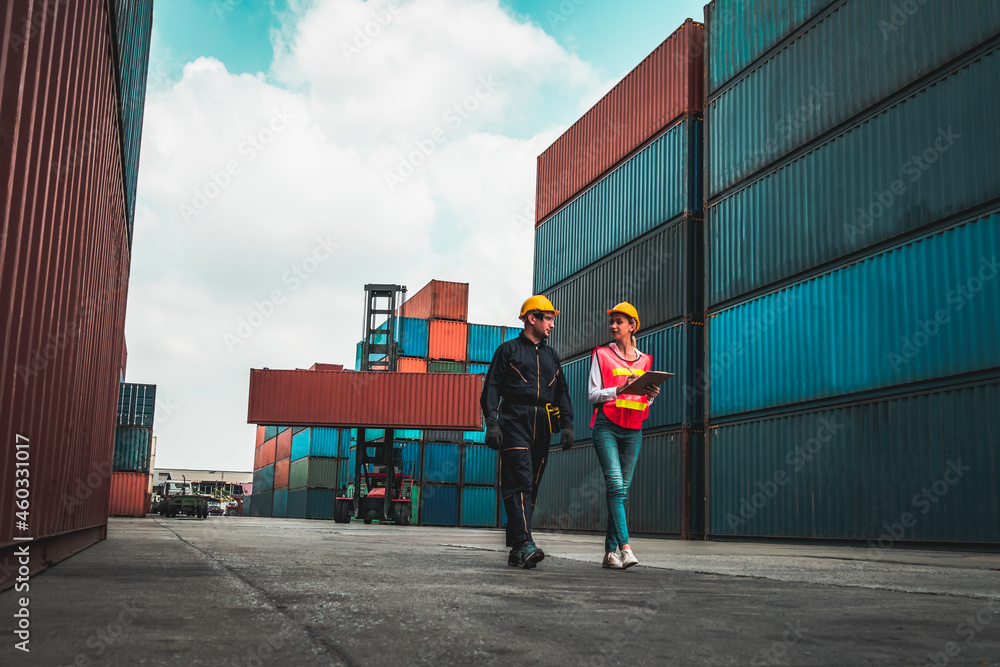 Industrial worker works with co-worker at overseas shipping container yard . Logistics supply chain management and international goods export concept . - obrazy, fototapety, plakaty 