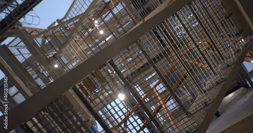 Industrial lattice metal staircase with orange metal railing goes up to the next floor 
