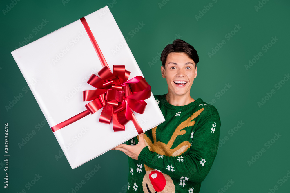 Photo of crazy funky guy hold big giftbox omg face wear deer ornament sweater isolated green color background Photo of crazy funky guy hold big giftbox omg face wear deer ornament sweater isolated green color background
