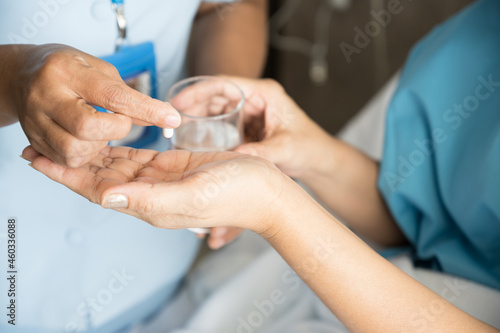 Close up of nurse hand putting white pill into patient hand.Sick female holding glass for taking medicines, antidepressant, painkiller or antibiotic.Pharmacy and healthcare concept