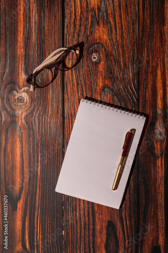 Notepad, pen and glasses for writing business ideas. Wooden background