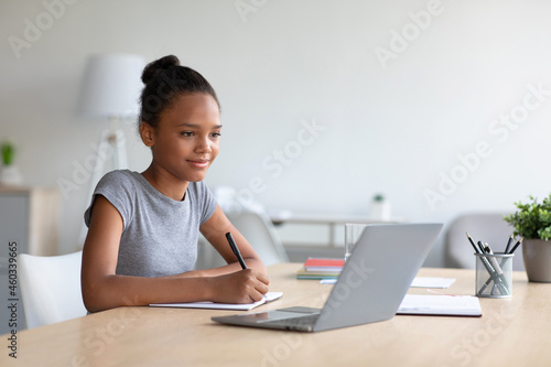 Smiling pretty smart teen african american girl student studying at home, watching online lesson on laptop