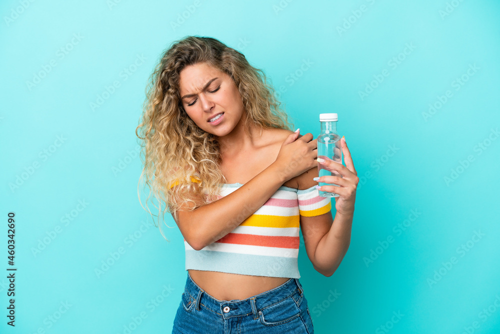 Young blonde woman with a bottle of water isolated on blue background suffering from pain in shoulder for having made an effort